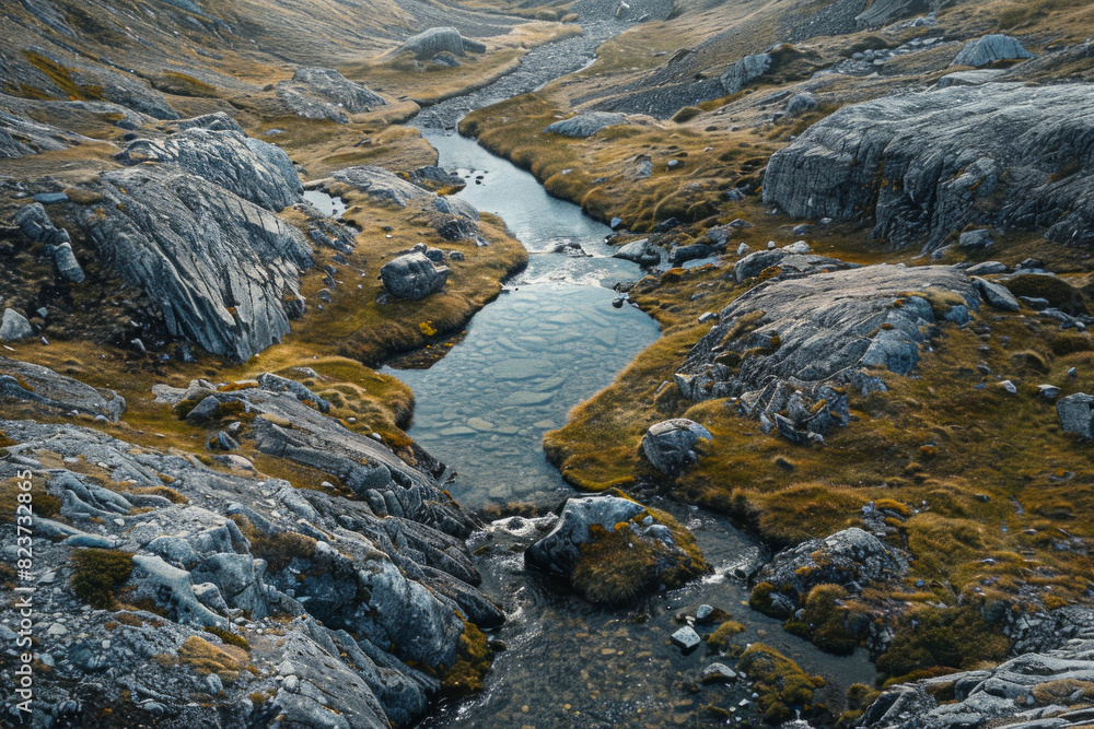 Aerial view of a narrow mountain stream winding through a rocky landscape. Focus on the simplicity of the clear water cutting through the rugged terrain. Aerial view of a narrow mountain stream winding through a rocky landscape. Focus on the simplicity of the clear water cutting through the rugged terrain.