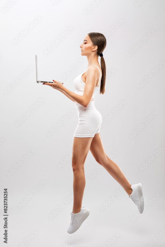 Obraz premium Slender dark-skinned female blogger in a white tracksuit against a white background. Healthy lifestyle, sports and diet.