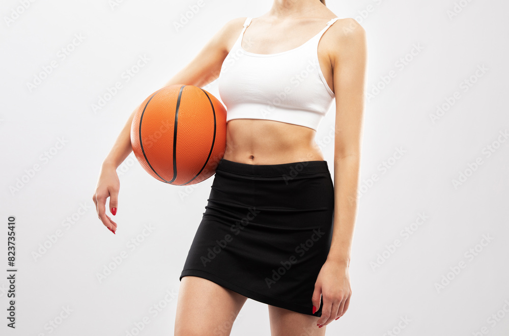 A beautiful slender girl athlete in shorts and in white top plays basketball.