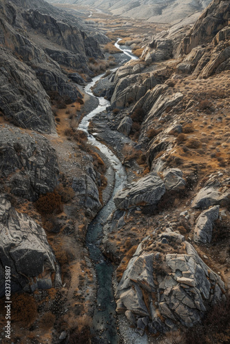 Aerial view of a narrow mountain stream winding through a rocky landscape. Focus on the simplicity of the clear water cutting through the rugged terrain.