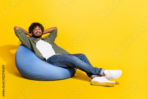 Portrait photo of young funny mexican guy in khaki shirt lying beanbag dreaming about better life isolated on yellow color background