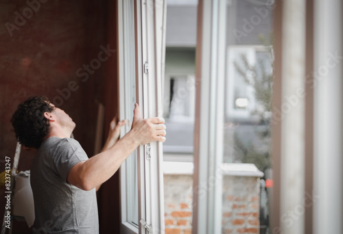 A young man installs a window frame with glass.