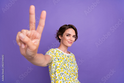 Portrait of pretty young woman demonstrate v-sign wear t-shirt isolated on purple color background photo