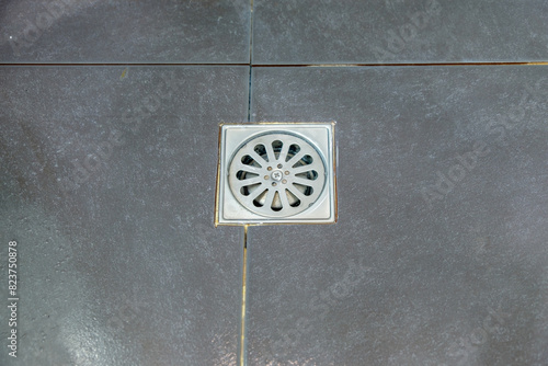 The metal drain cover on the black floor tiles.