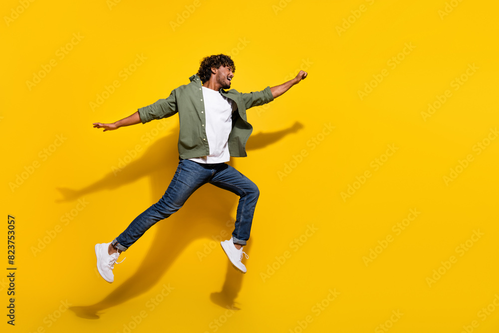 Portrait photo of young funny mexican guy in khaki shirt and jeans jumping running motivated isolated on yellow color background