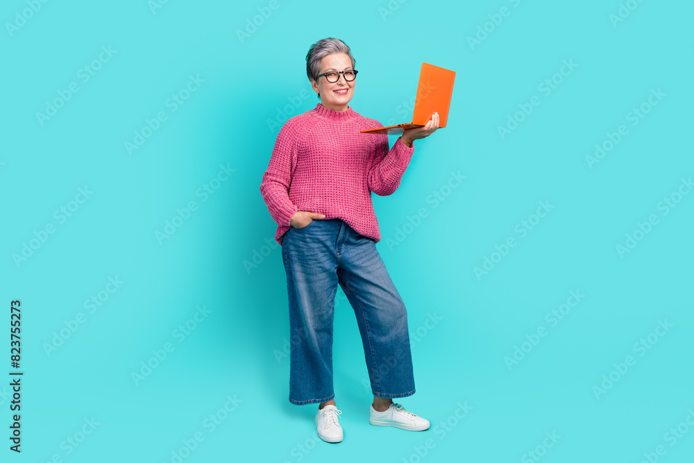 Full length photo of clever good mood woman wear pink sweater denim pants hold laptop arm in pocket isolated on teal color background Full length photo of clever good mood woman wear pink sweater denim pants hold laptop arm in pocket isolated on teal color background