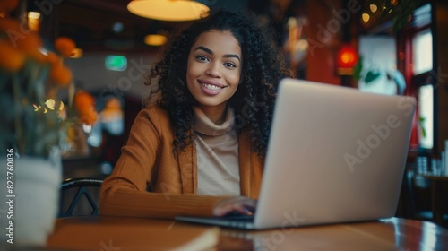 A beautiful mulatto young smiling woman working on a laptop, a freelance girl or a student at a computer in a cafe.