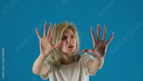 Young woman student tries to stop communication with hand gestures on blue background. Emotional female wants to prevent dispute photo