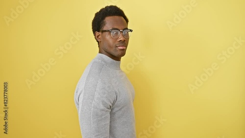 Confident young african american man with glasses flaunting his natural smile in profile pose, standing out against a yellow isolated background photo