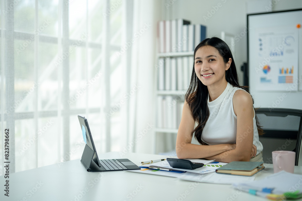 Fototapeta premium A woman is sitting at a desk with a laptop and a calculator