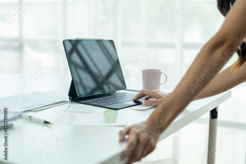 A woman is typing on a laptop while holding a cup of coffee