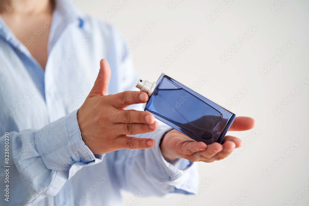 Hands in a blue shirt hold a blue bottle of perfume. Hands in a blue shirt hold a blue bottle of perfume.