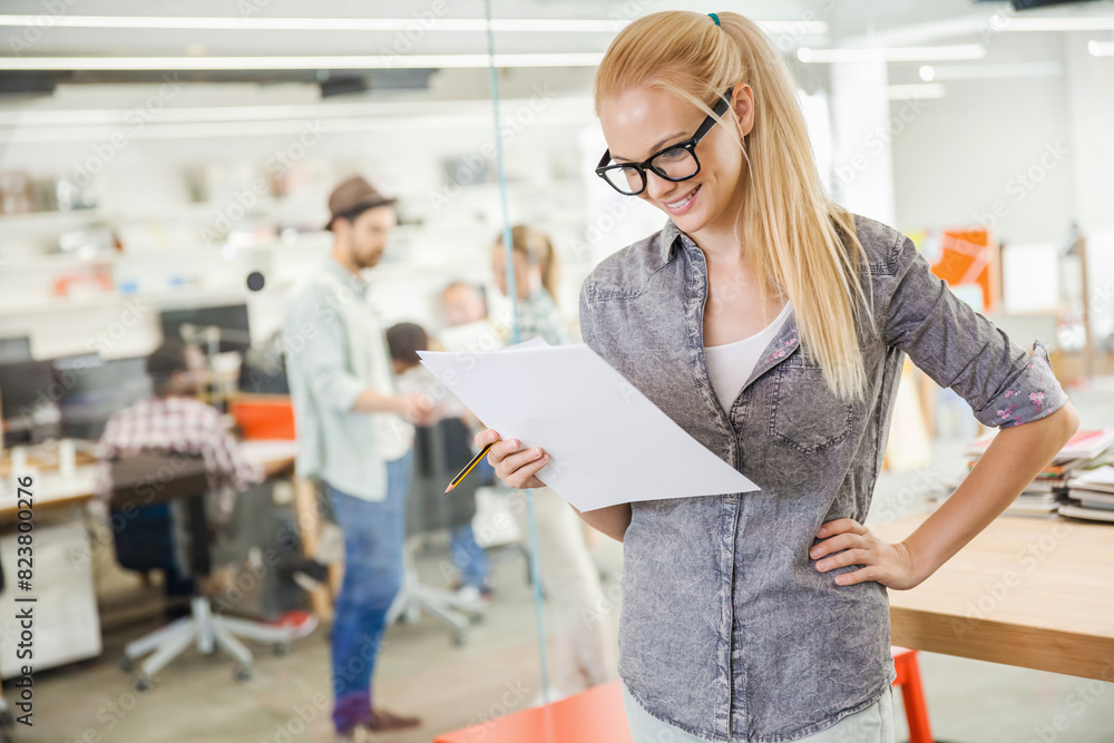 Smiling young woman reading document in busy office Smiling young woman reading document in busy office