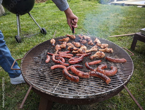 Tableau sur toile Cozinheiro a assar carne e salsichas no assador na grama do quintal, churrasco n