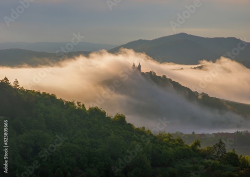 Natural scenery with fog and a historical building obscured in the fog. Beautiful natural view, wet weather. Scenic lighting sky with clouds and landscape. Calvary over clouds in Banska Stiavnica. © Ivan