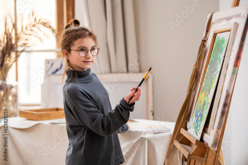 A girl with glasses paints a picture on canvas.