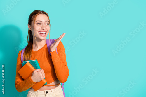 Portrait of overjoyed woman wear orange crop top rucksack hold book look at discount empty space isolated on turquoise color background