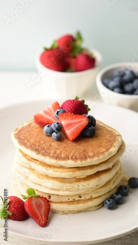 pouring syrup on piled pancake with strawberries and bluberries
