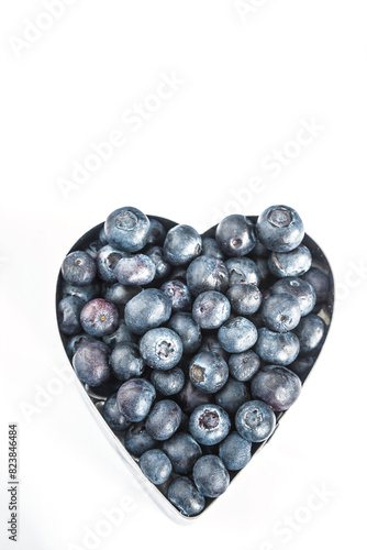 Heap of blueberries in heart shaping bowl on white background with space for text