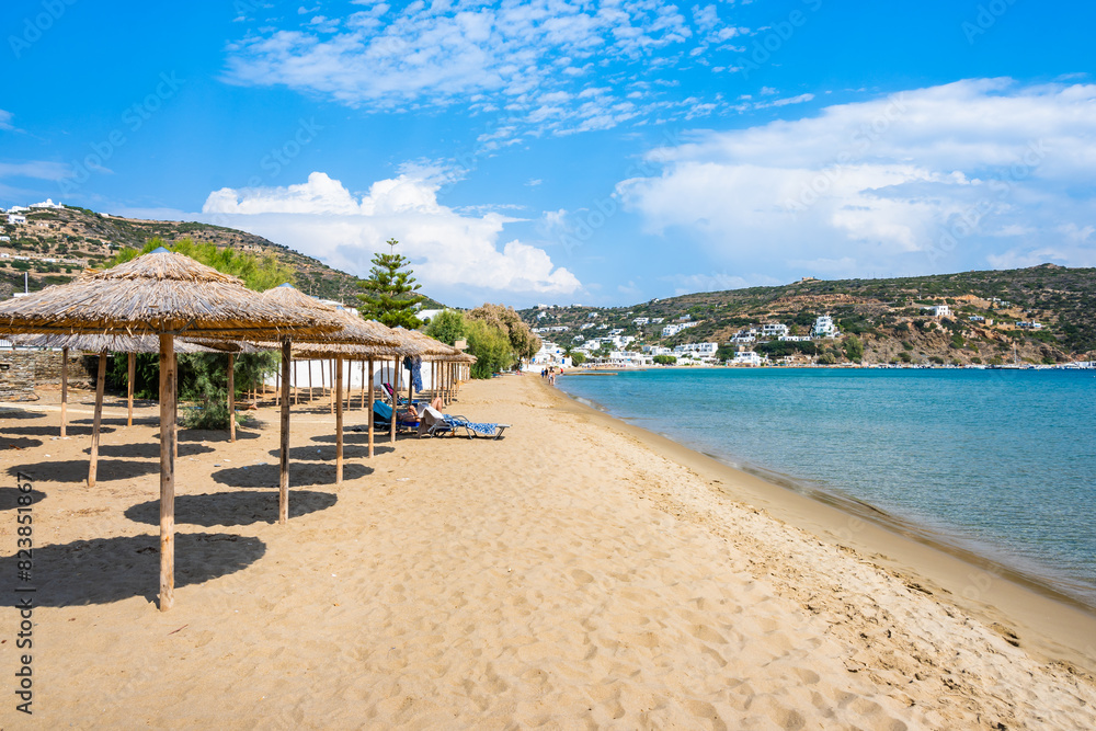 Sun loungers and umbrellas in Platis Gialos village on sandy beach with sea view, Sifnos island, Greece