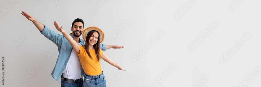 Young couple in love pretending airplane flight, spreading hands like wings, having fun while posing over light studio wall, looking and smiling at camera, copy space Young couple in love pretending airplane flight, spreading hands like wings, having fun while posing over light studio wall, looking and smiling at camera, copy space