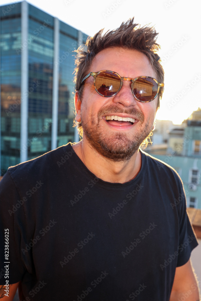 Portrait man smiling and wearing sunglasses in rooftop during sunset Portrait man smiling and wearing sunglasses in rooftop during sunset