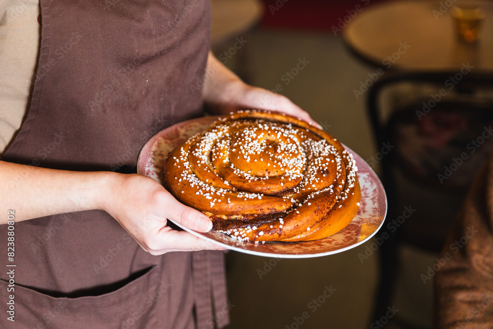 © Diego Martin/Stocksy - Portrait of waiter serving giant cinnamon bun © Diego Martin/Stocksy - Portrait of waiter serving giant cinnamon bun
