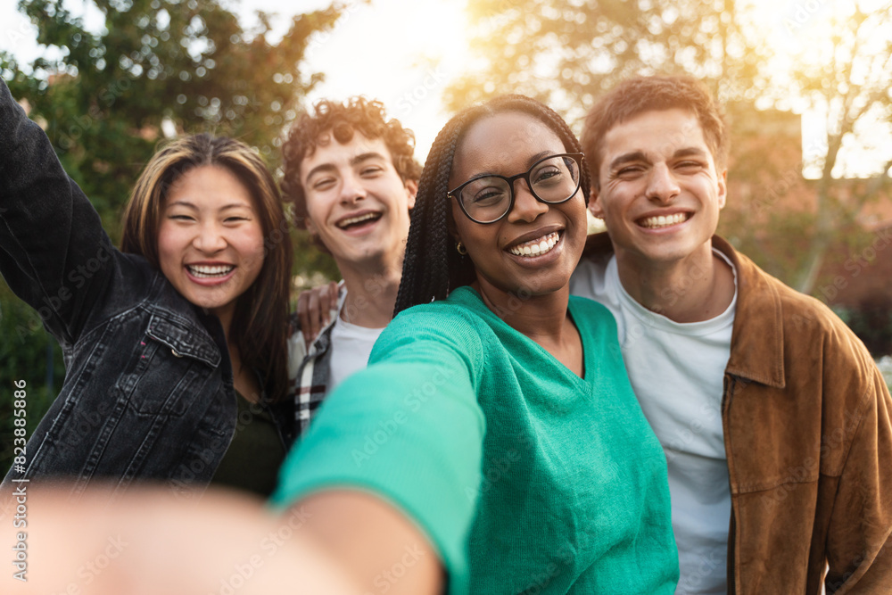 African girl with eyeglasses with four cheerful generation z friends taking a selfie photo at sunset