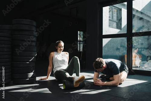 Fitness coach instructing sportswoman foam rolling calves