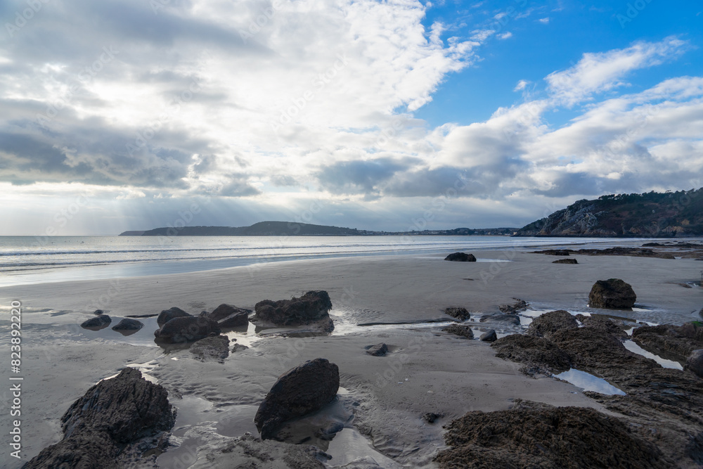 Plage sauvage de la presqu'île de Crozon, joyau breton baigné par la mer d'Iroise, avec sable fin, falaises, et rochers sur le sable mouillé à marée basse.