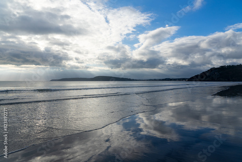 Plage sauvage de la presqu   le de Crozon  joyau breton baign   par la mer d Iroise  avec sable fin et falaises  o   les reflets du bleu du ciel et le blanc des nuages se posent sur le sable mouill  .