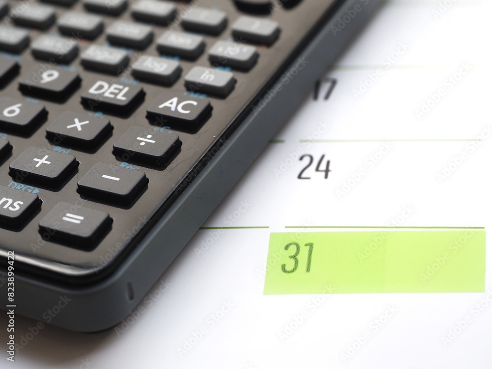 Close-up of a monthly calendar showing the date 31 next to a calculator. Represents the 31st end of the month and a business concept Close-up of a monthly calendar showing the date 31 next to a calculator. Represents the 31st end of the month and a business concept