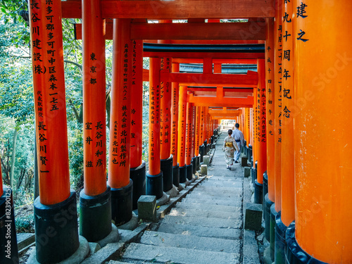 Young couple wearing kimonos walking along orange torii gates walkway photo