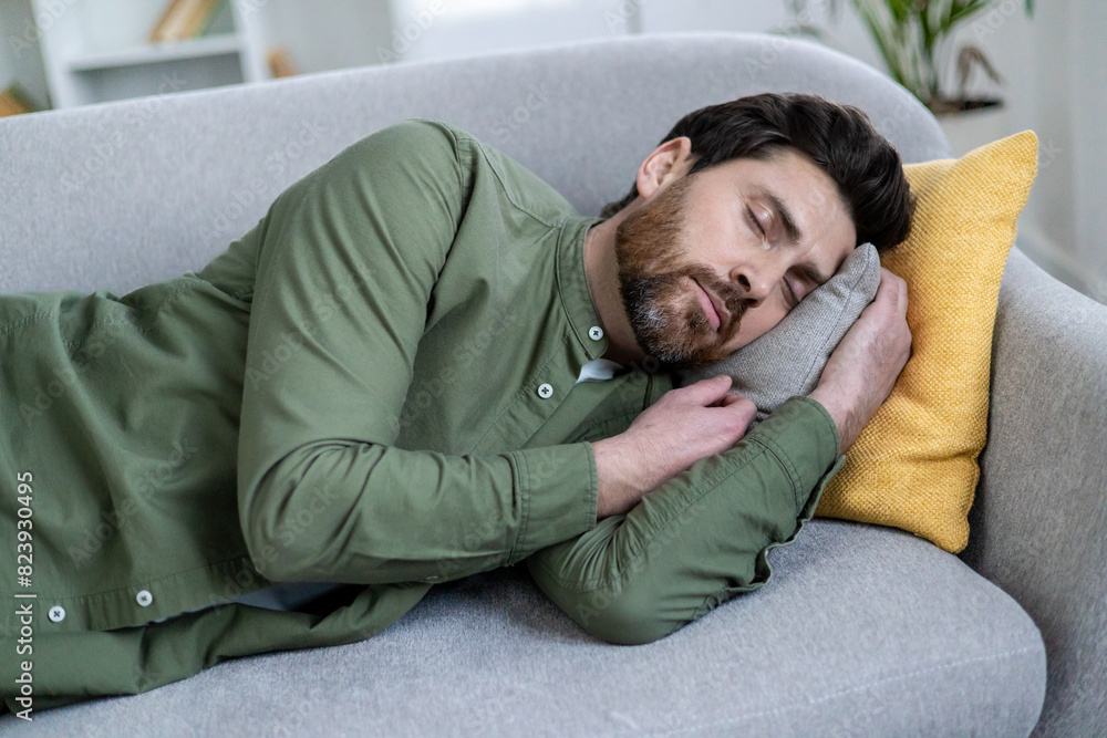 Bearded man peacefully napping on a gray sofa with yellow and gray pillows in a cozy living room environment. Bearded man peacefully napping on a gray sofa with yellow and gray pillows in a cozy living room environment.
