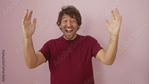 Joyful young hispanic man in a t-shirt, eyes closed, arms aloft in a lunatic celebration of success! winner gone mad over crazy win, isolated on pink background. photo