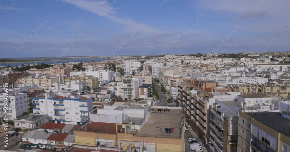 Panoramic cityscape of Sanlúcar de Barrameda with house rooftops on the street seen from above with ocean in the background tilt up