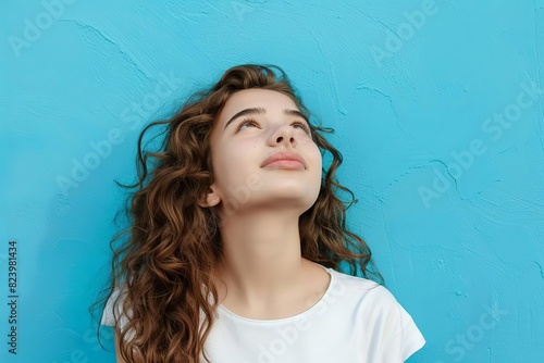 curious cheerful brownhaired girl looking up bright blue background positive emotion portrait photo