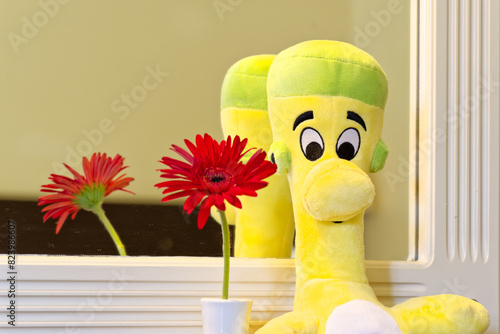 A stuffed toy is placed in front of a mirror next to some flowers
