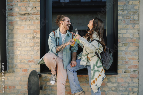 Smiling trendy couple sitting on window outside and having drinks. photo