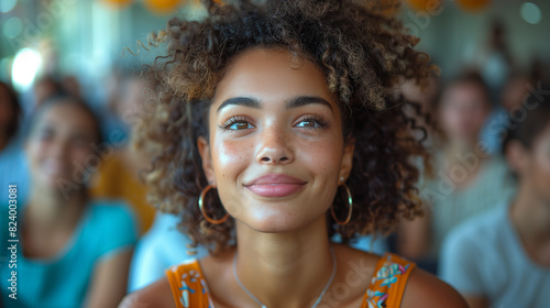 A woman with curly hair smiles while standing in front of a group of people