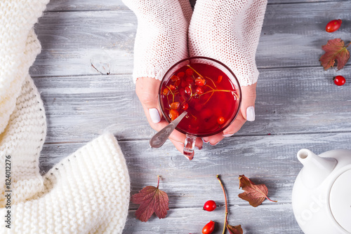 Hands of a woman in a sweater holding a cup of hot tea on a gray wooden background with copy space. Top view