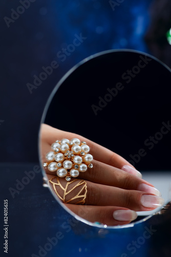 A womans hand adorned with a pearl ring is reflected in a mirror