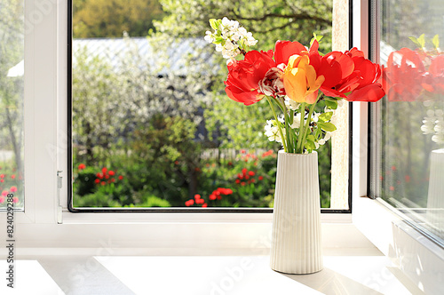 Beautiful tulips in a vase on an open sunny window. The concept of home coziness, comfort and home office. Abstract spring floral arrangement, banner, summer background, selective focus..