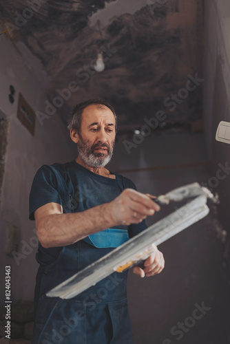 Senior man working with spatula and plaster while renovating interior , makes repairs in the house. 
