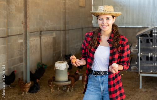 Portrait of happy young woman farmer standing in hen house with fresh chicken eggs in hands photo