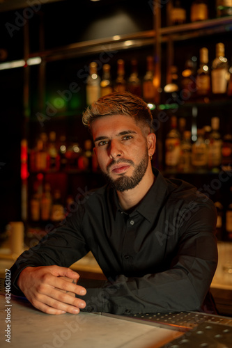 Young elegant barman working behind a bar counter mixing drinks