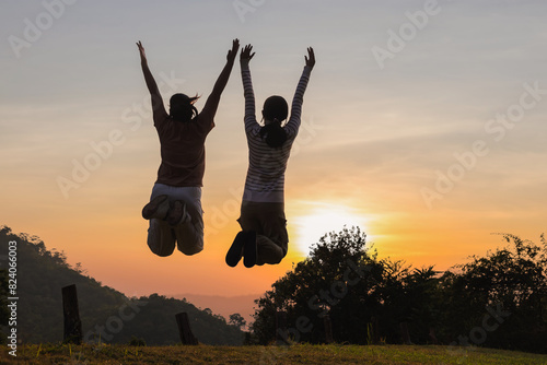 Silhouette happy two women friends jumping on mountain sunset sky background