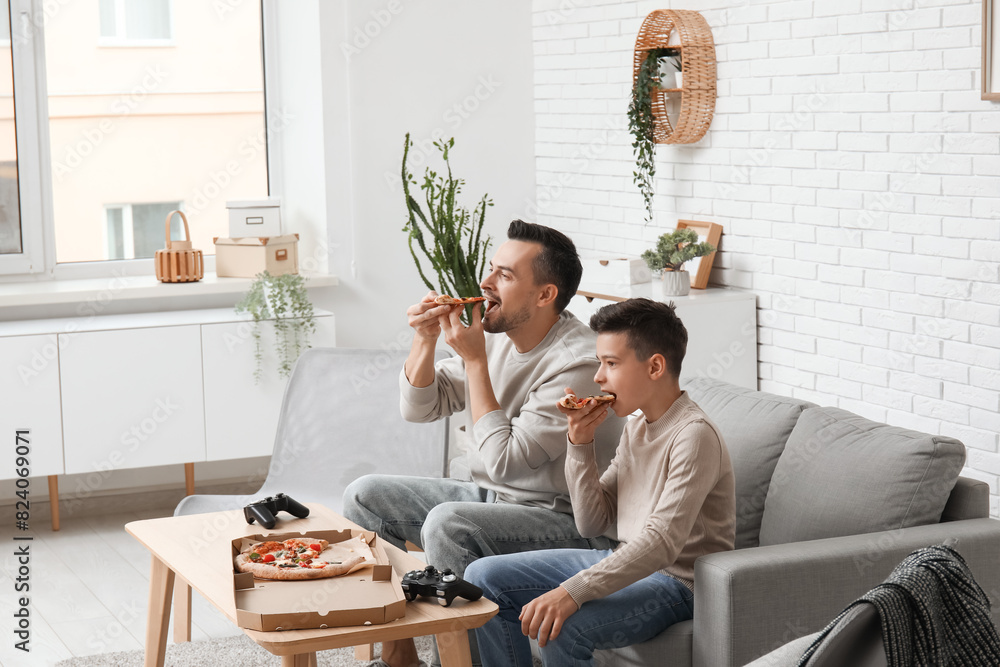 Father and his little son eating pizza on sofa at home Father and his little son eating pizza on sofa at home