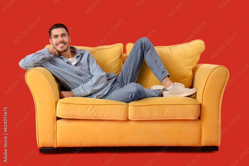 Handsome young happy man resting on sofa against red background Handsome young happy man resting on sofa against red background