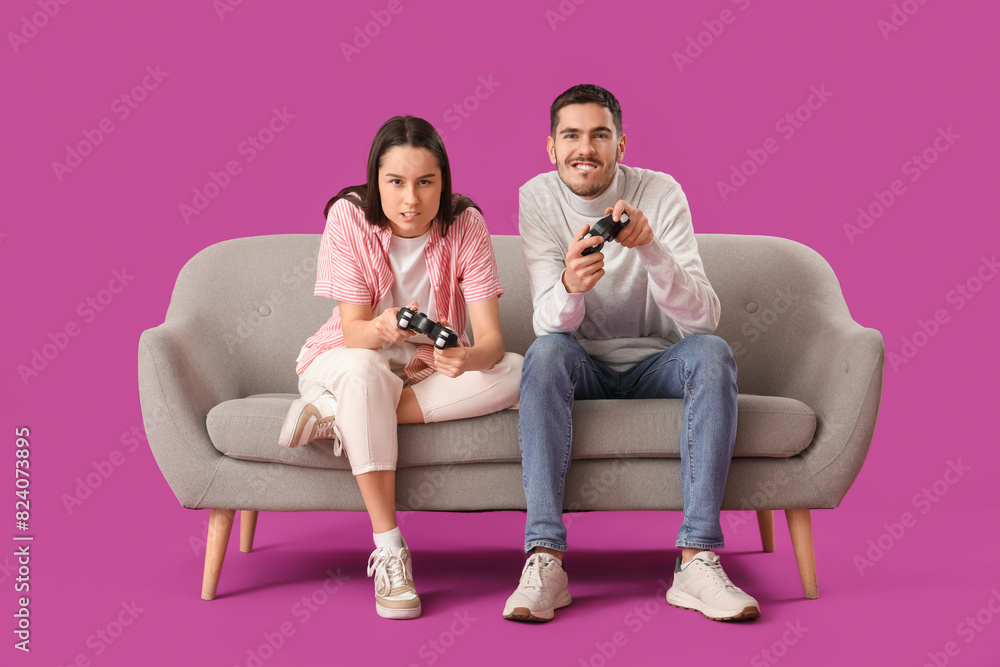 Beautiful young couple playing video games on sofa against purple background Beautiful young couple playing video games on sofa against purple background